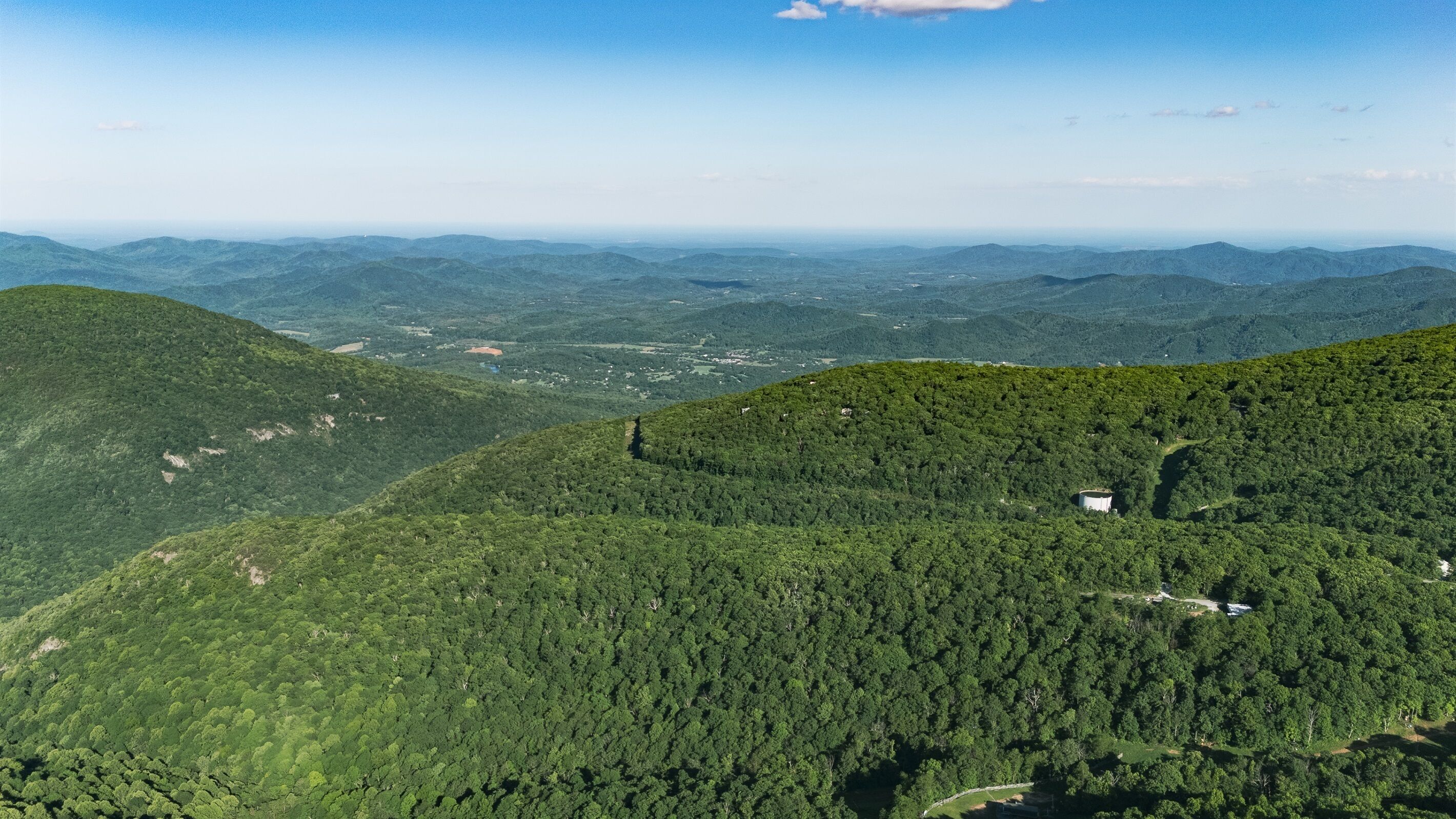 Paisaje montañoso con bosque denso, un edificio pequeño y una vista distante de un valle.