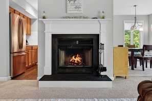 A modern kitchen with a built-in stainless steel refrigerator, wooden cabinets, and a white fireplace with a fire.