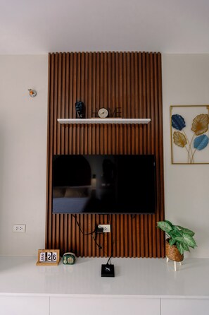 Ett modernt vardagsrum med en platt-TV som är monterad på en väggpanel av trä, en hylla med dekorativa föremål, en klocka och en krukväxt.