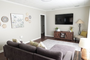 A living room with a sofa, a TV, a wooden entertainment unit, and decorative wall art.