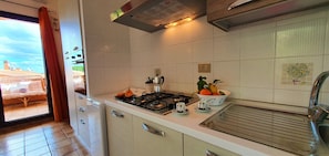 A kitchen with white cabinets, a stove, a sink, and a window with a view of a building. - Sardinia Stella Corallo-Lovely Apartment sea view (Sardegna)