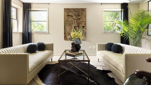 A living room with two beige sofas, a glass coffee table, and a large wall painting.