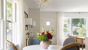 A dining area with a round table, four chairs, a vase of flowers, and a chandelier.