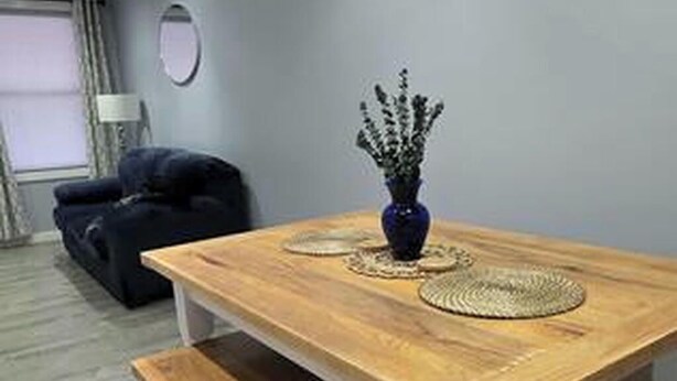 A dining area with a wooden table and benches, a vase with flowers, and a black sofa. - Work, Crew & Family Stay Near Downtown Reading (Reading)