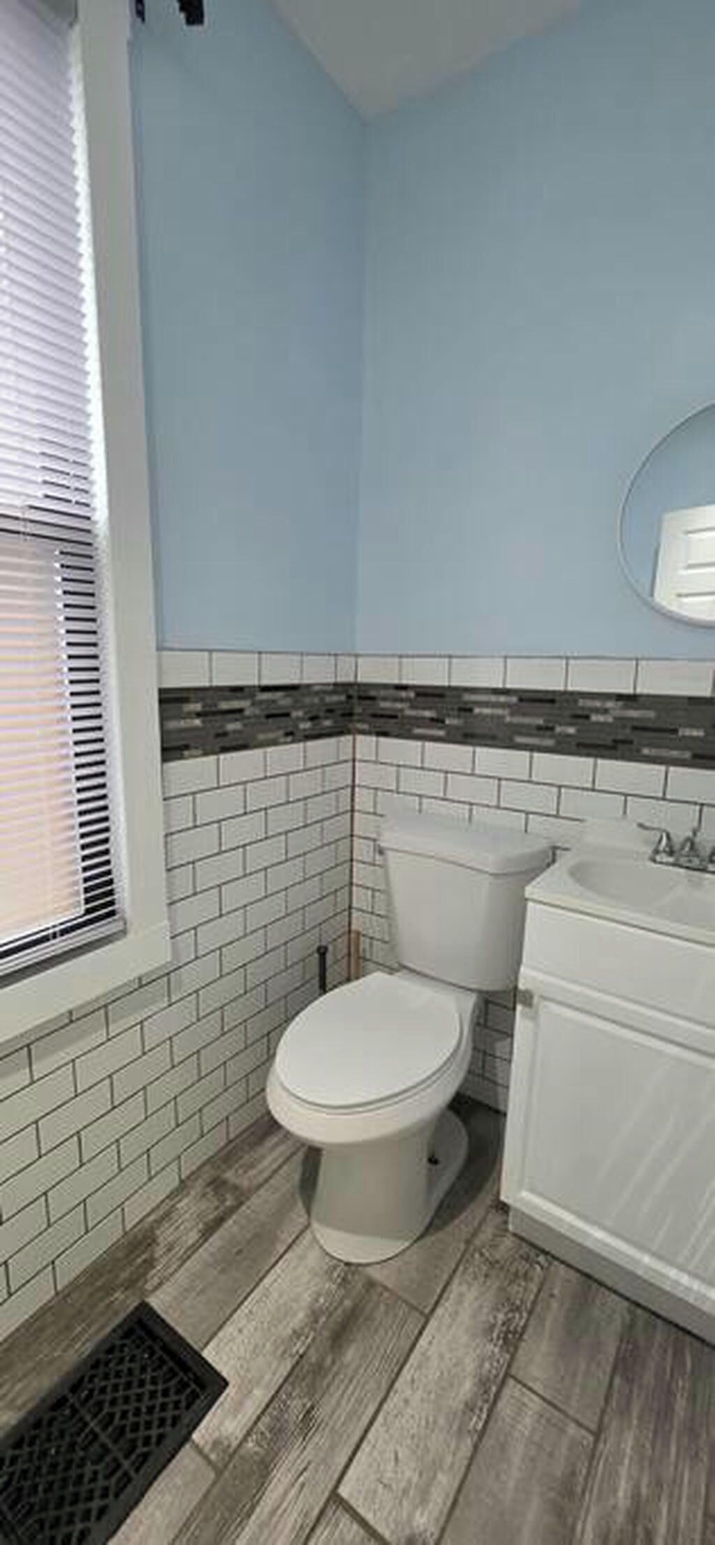 A bathroom with a white toilet, a sink, and a window with blinds.