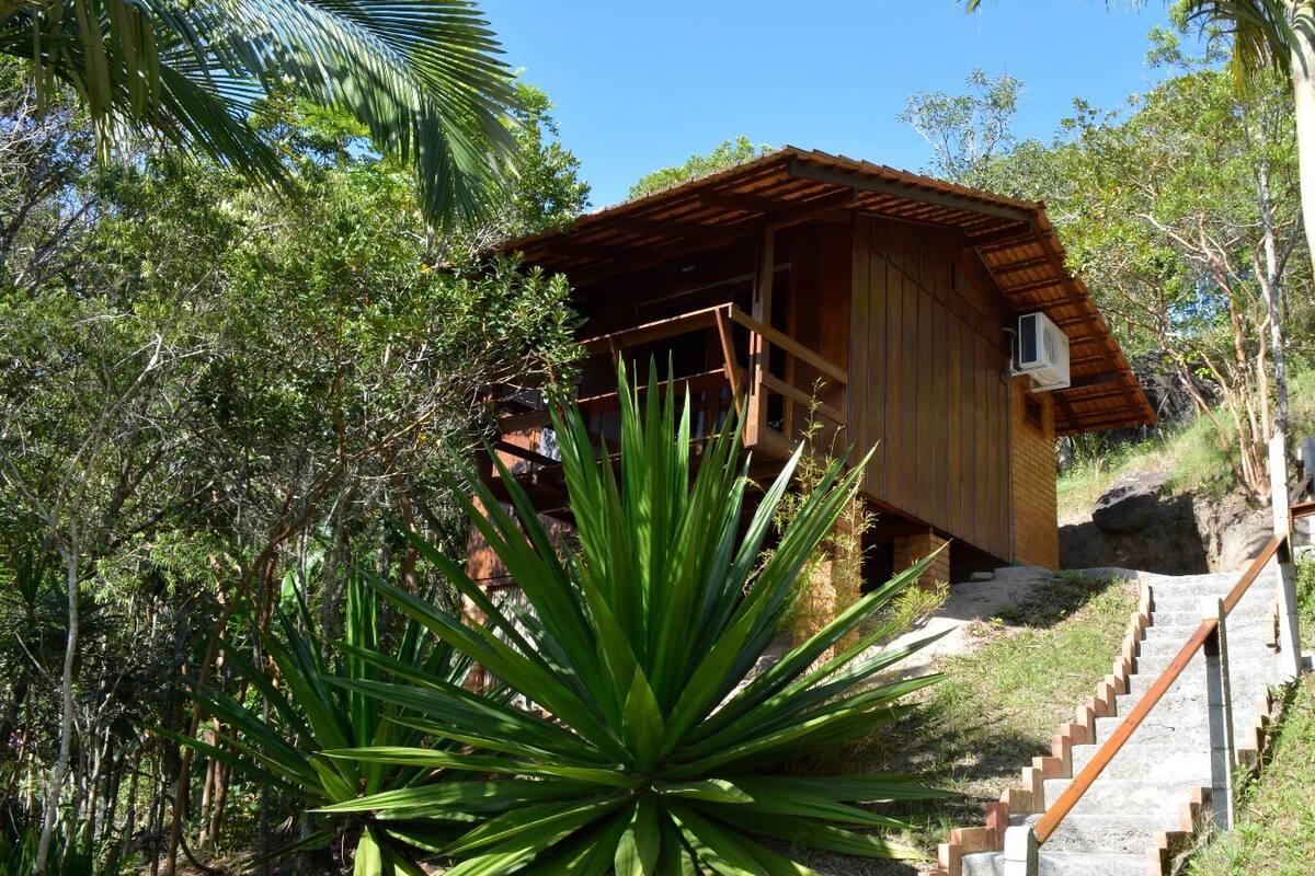 Une cabane en bois, dotée d’un toit en pente, entourée d’une végétation luxuriante, et un escalier menant à son entrée.