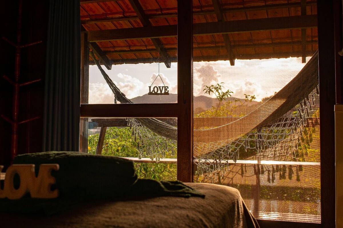 Une chambre avec un lit, un hamac et une vue sur une maison ornée d’une enseigne « LOVE ».