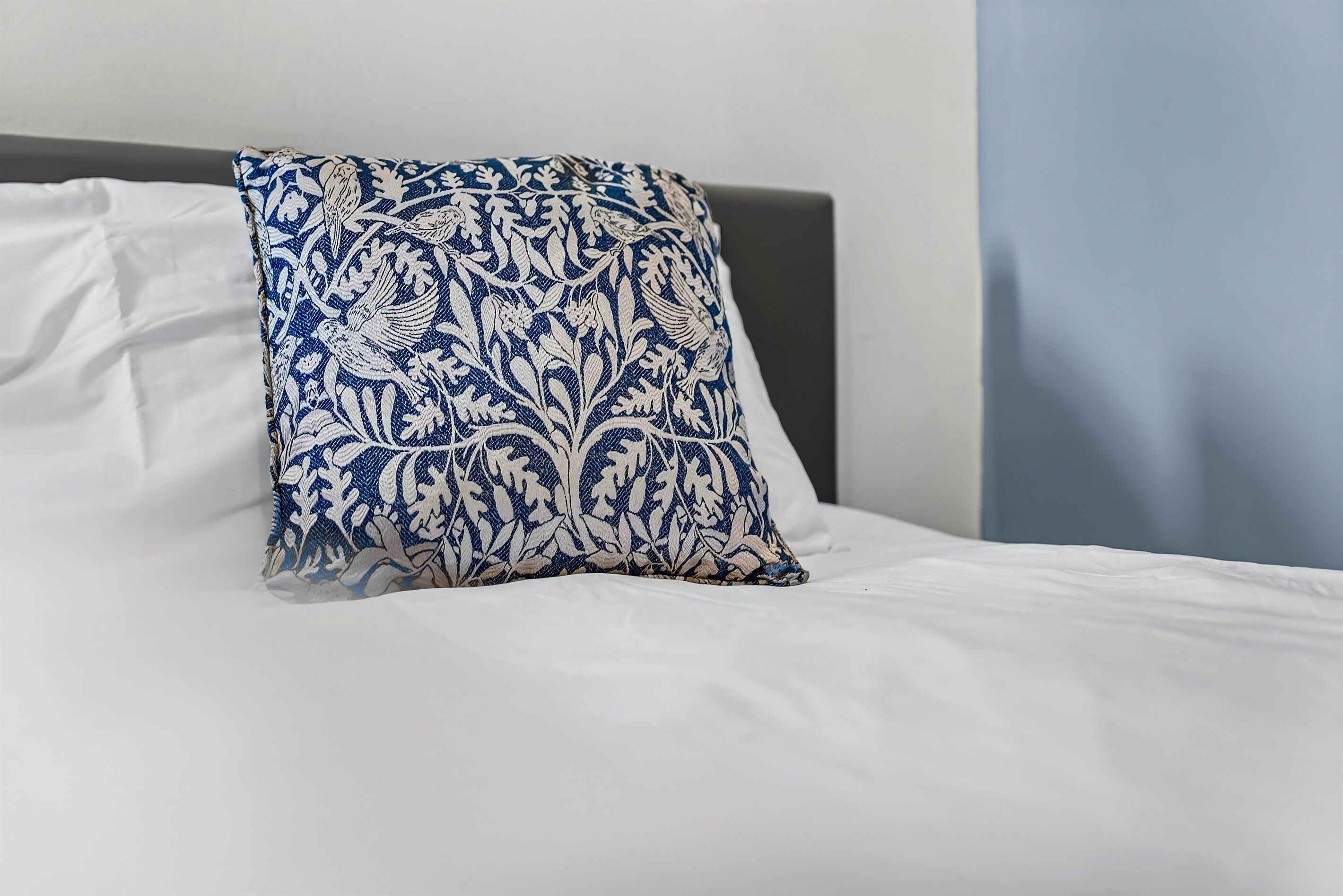 A bed with white bedding and a blue and white patterned pillow.