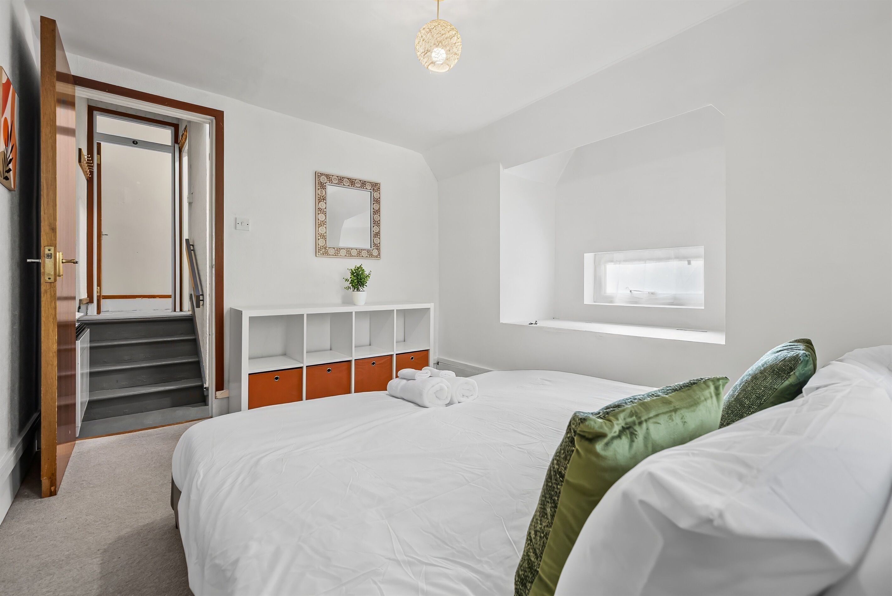 Una camera da letto con un letto, una finestra, uno specchio, una scala e una scaffalatura.