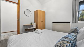 A bedroom with a bed, a wooden wardrobe, a desk with a chair, and a window with curtains.