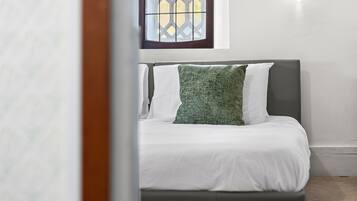 A bedroom with a bed, white bedding, a green pillow, a window with a lattice design, and a wall-mounted light fixture.