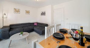 A modern living room with a sectional sofa, a small round table, and a dining area with a wooden table set for two.