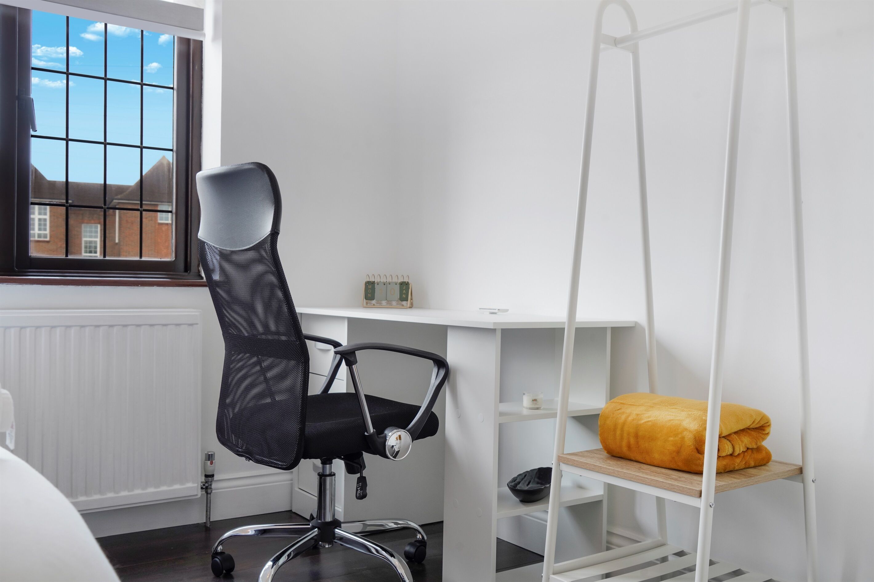 Un espace de bureau moderne comprenant un fauteuil de bureau noir, un bureau blanc, une étagère blanche et un fauteuil suspendu.