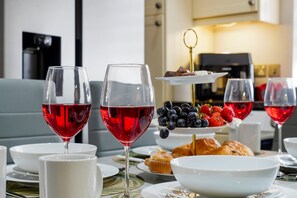 Una mesa de comedor con copas de vino, un plato de pasteles y una cafetera al fondo.