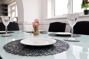 Une table à manger dressée avec des assiettes, des couverts et de la verrerie, agrémentée d’un centre de table décoratif et offrant une vue sur l’extérieur.