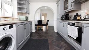 A modern kitchen with grey cabinetry, a built-in washing machine, a microwave, and a stove.