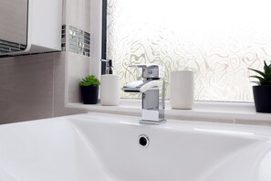 Une salle de bain avec un lavabo blanc, un robinet chromé et une fenêtre ornée de verre dépoli.