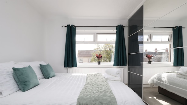 A modern bedroom with a large bed, green curtains, a view of the outside, and a mirror reflecting the room.