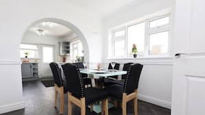 A dining area with a round table and six chairs, an arched doorway leading to a kitchen, and a window with a view of the outside.