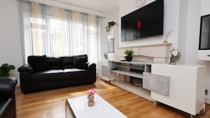 A modern living room with a black sofa, white entertainment unit, and a flat-screen TV mounted on the wall.