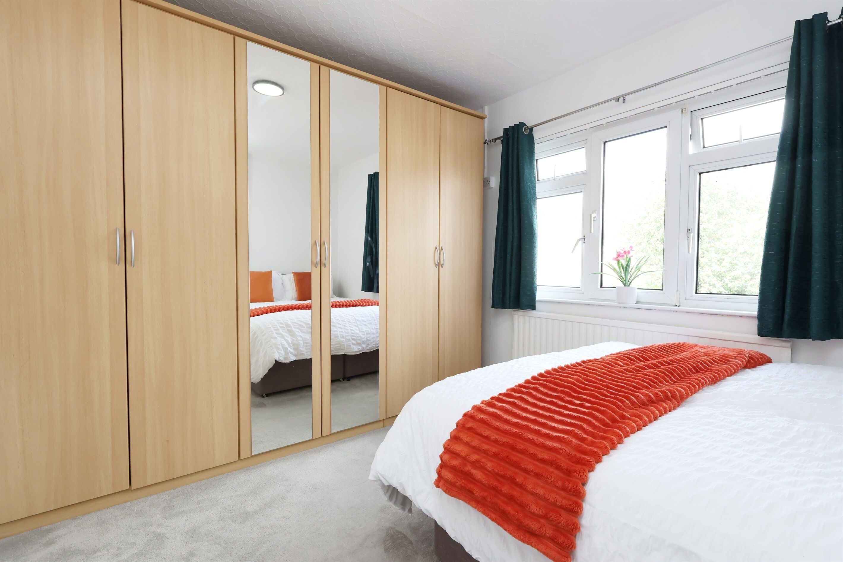 A bedroom with a large wardrobe, a bed with a white and red blanket, and a window with curtains.