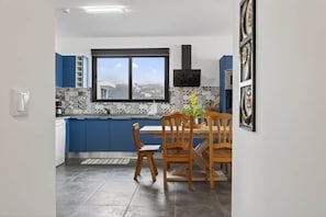 A modern kitchen with blue cabinets, a dining table with chairs, and a window with a city view. - Sea View Apartment in Calheta, Madeira | Casa Teixeira (Estreito da Calheta)