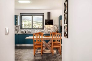 Una cocina con mesa y sillas, ventanal con vistas y salpicadero de azulejos.