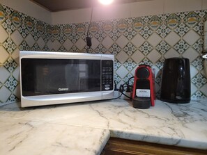 Een keuken met een Galanz magnetron, een rode koffiezetapparaat en een zwarte waterkoker op een marmeren aanrecht.