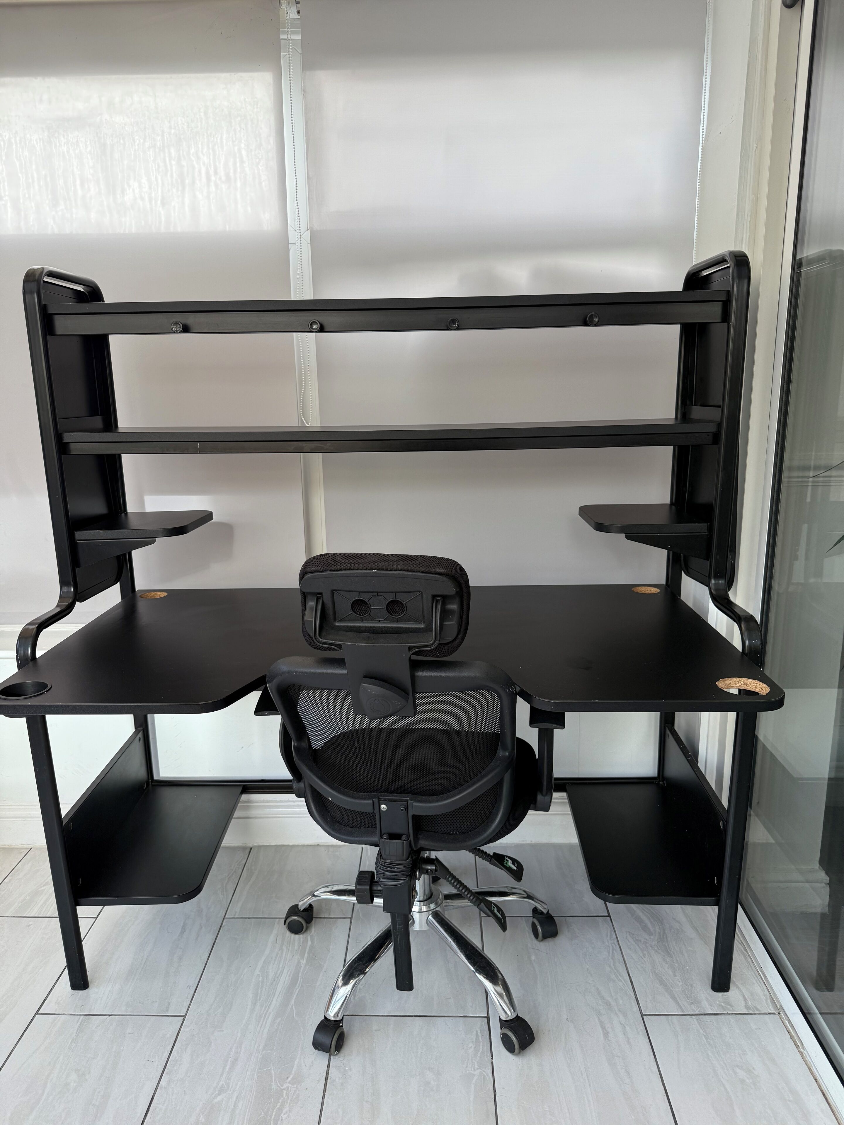 Een zwarte bureaustoel met een mesh rugleuning en een bureau met twee planken en een toetsenbordlade.