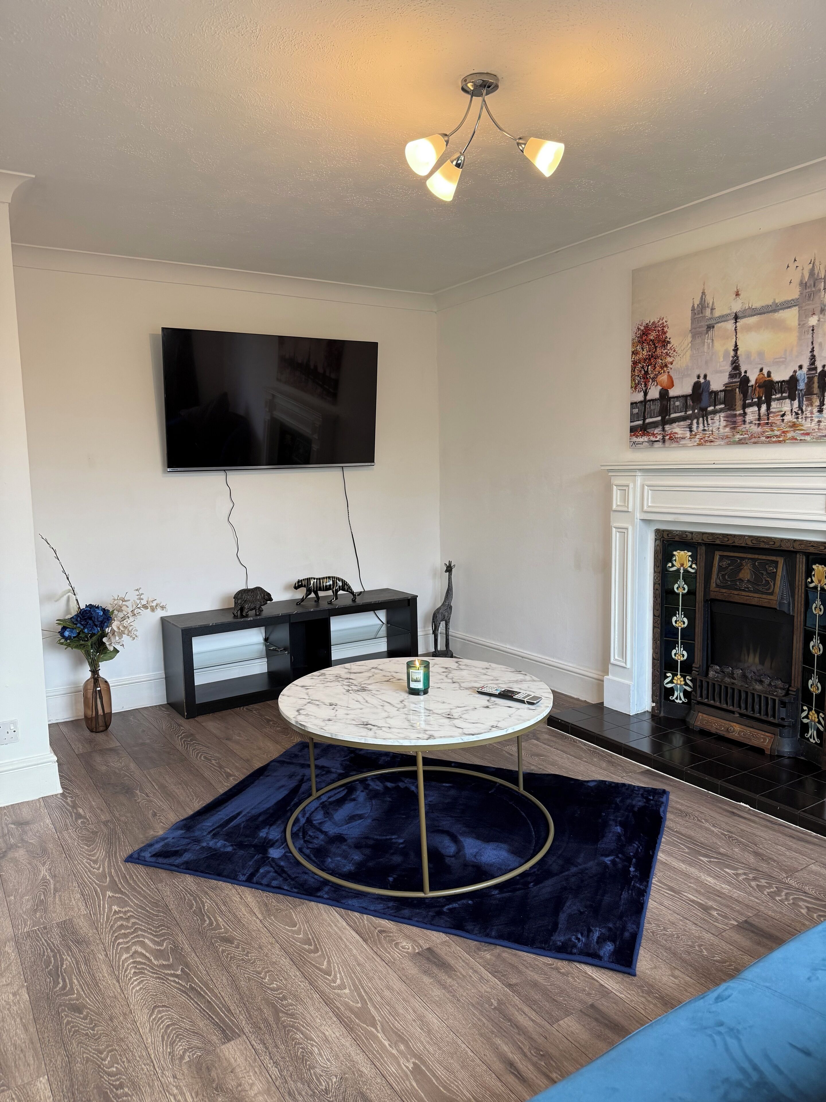 A living room with a flat-screen TV, a fireplace, a round marble coffee table, and a blue rug.