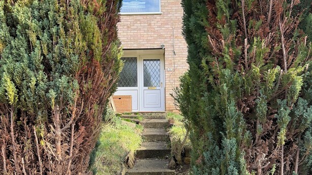 A pathway leading to a house with a brick facade, a white door, and a window. - Stylish 3-Bed with Smart TVs, Parking & Workspace (Kettering)