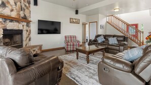 Ein Wohnzimmer mit Ledersofas, einem Steinkamin, einem Flachbildfernseher, einem Deckenventilator und einer Treppe.