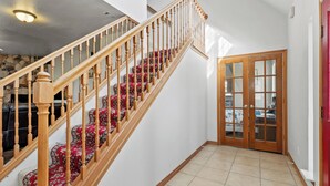 Eine Treppe mit hölzernen Geländern und roten Teppichstufen führt zu einem Raum mit einer Holztür und einem gefliesten Boden.