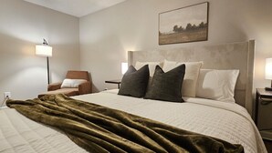 Een keurig ingerichte hotelkamer met een groot bed, een stoel, twee nachtkastjes met lampen en een schilderij aan de muur.