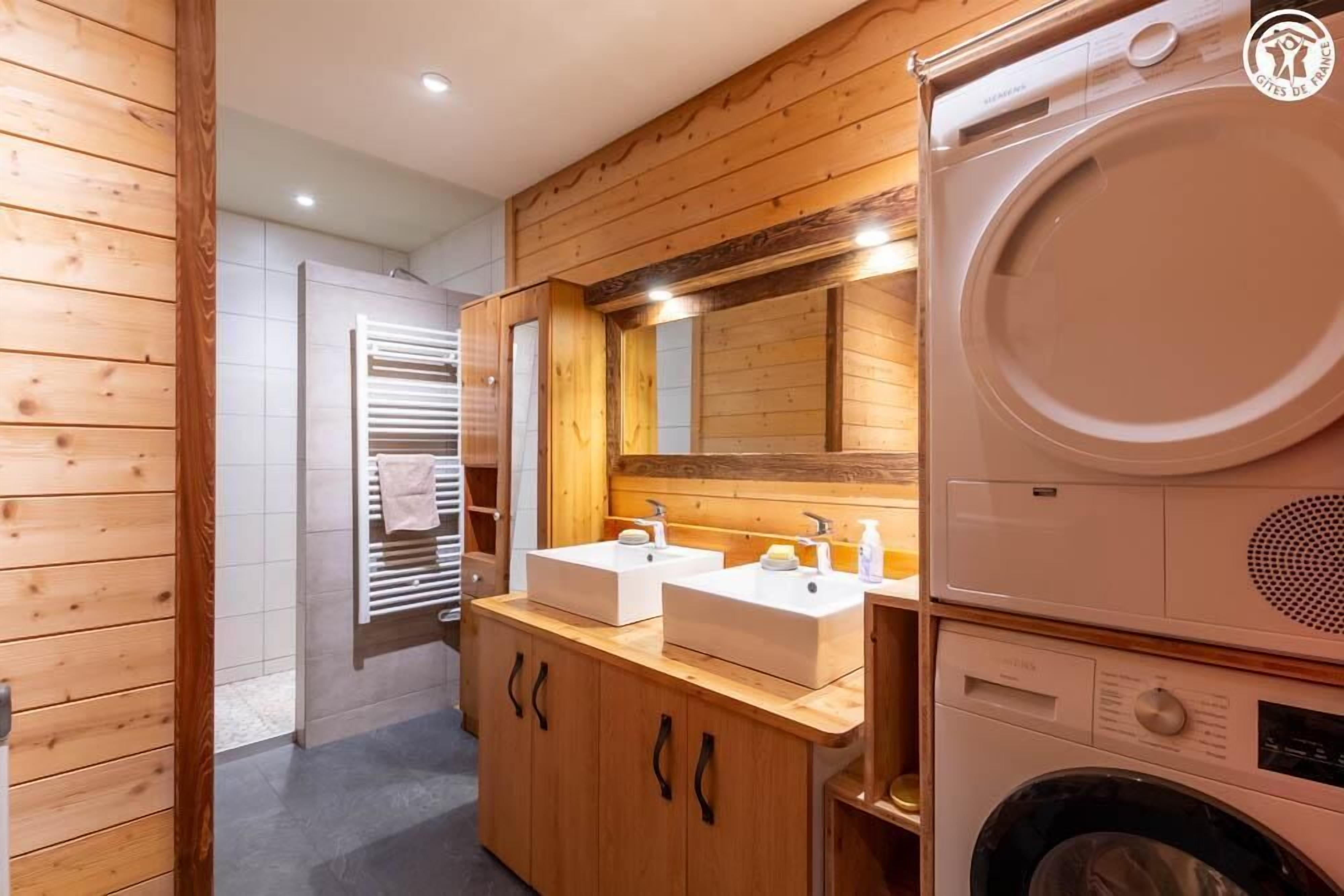 A modern bathroom with wooden paneling, a double sink vanity, a large mirror, and a built-in washing machine.