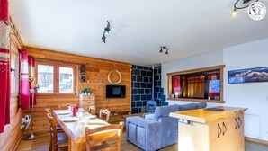 Een knus logies in houten chaletstijl met een houten eettafel, een bank en een kitchenette met televisie en open haard.