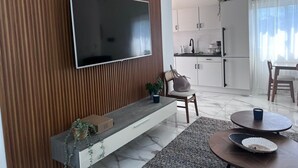A modern living room with a flat-screen TV mounted on a wooden wall, a built-in bench with a plant, and a dining area with a round table and chairs. - Breakview Penthouse 3BR  Retreat @ Encuentro Beach (Cabarete)