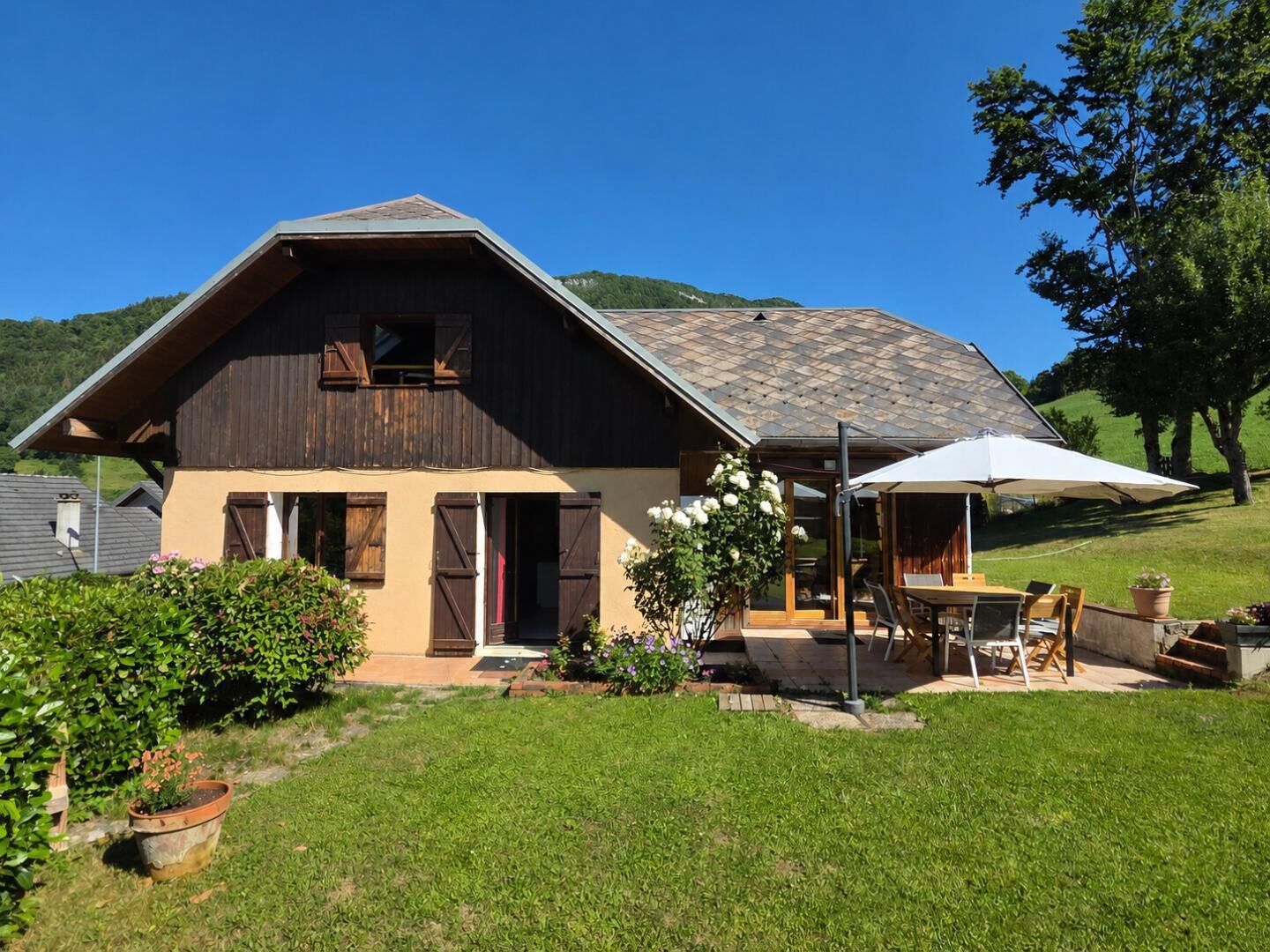 A two-story house with a sloped roof, wooden shutters, and a patio with outdoor furniture.