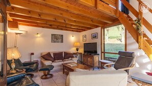 A cozy living room with a wooden ceiling, a sofa, a television, and a dining area. - GITE DES FONTANETTES (LA COMPOTE)