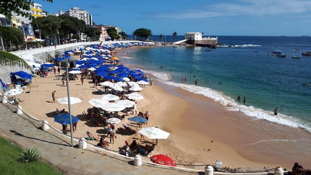 Een strand met parasols en mensen.