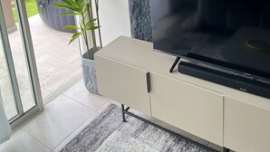 Ett modernt vardagsrum med en platt-TV, en vägg med stenliknande struktur, en skjutdörr i glas som leder ut till en trädgård och en krukväxt.