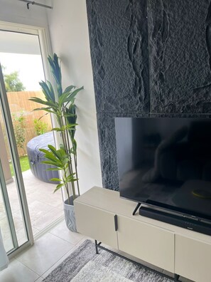 Ein modernes Wohnzimmer mit Flachbildfernseher, einer Wand mit Steinoptik, einer Schiebeglastür, die in einen Garten führt, und einer Topfpflanze.