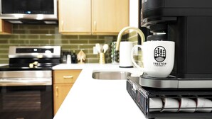 A kitchen with a coffee machine, a white mug with a logo, and a microwave.