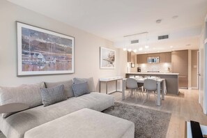 Un salon moderne avec un canapé gris, un coin repas comprenant une table et des chaises, et une cuisine dotée de meubles en bois et d’un four à micro-ondes.