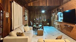 Ein gemütliches Wohnzimmer mit Holzboden, einer Couch, einem Couchtisch und einem an der Wand befestigten Fernseher.