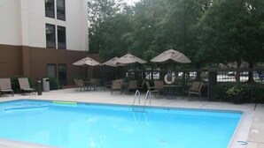 A rectangular pool with a ladder, surrounded by lounge chairs and umbrellas, with a building in the background.