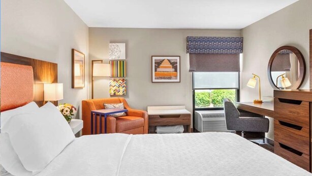 A hotel room with a bed, a desk, a chair, a sofa, and a window with a view.
