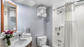 A bathroom with a vanity, toilet, shower, and a mirror with a geometric patterned wall.