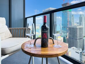 Een ronde houten tafel met een fles Apothic Red wijn en twee glazen op een balkon met uitzicht op een stadsbeeld.