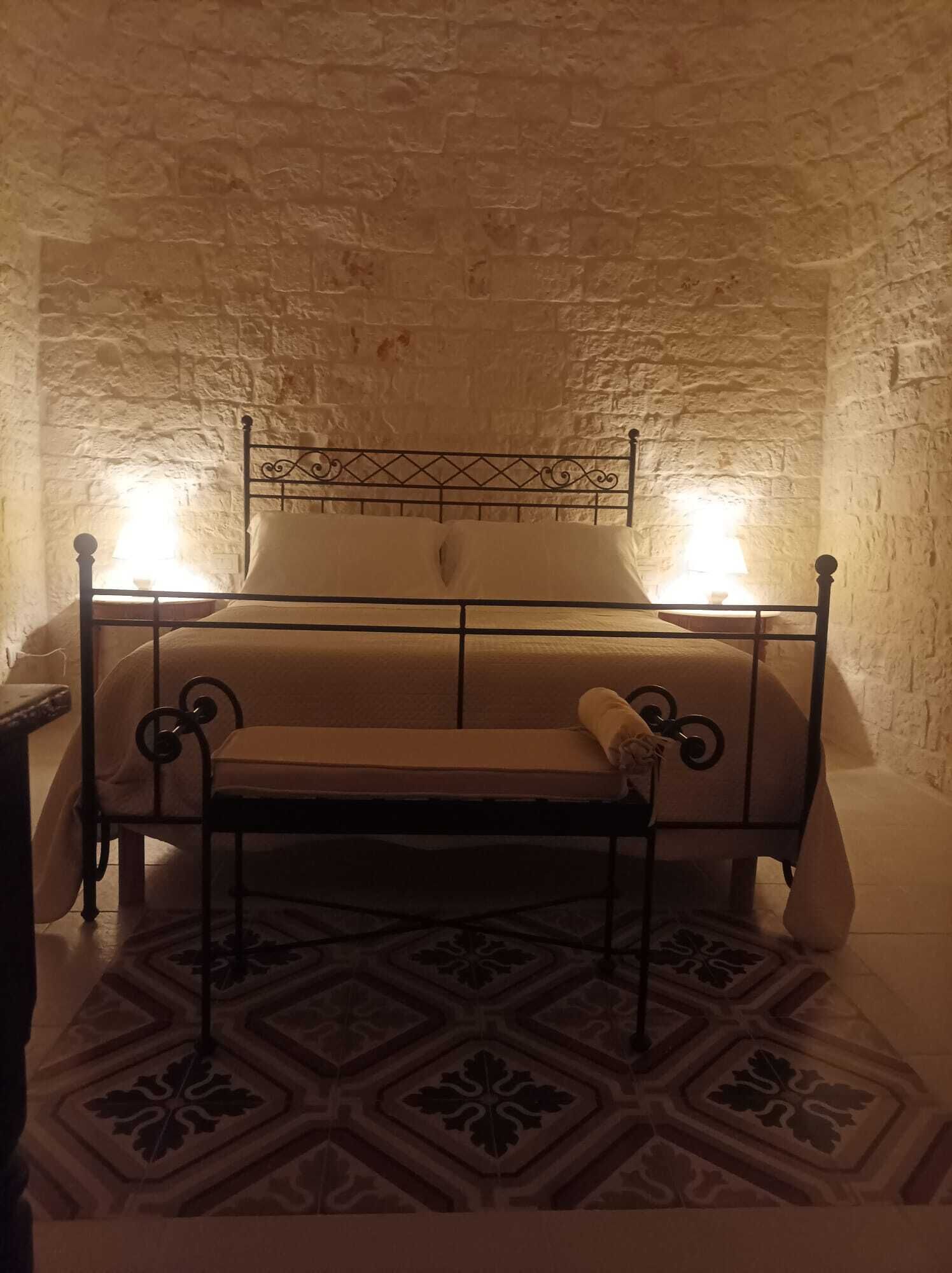 A bed with a metal frame and a headboard, positioned against a stone wall.